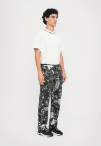 Camiseta blanca de manga corta con texto negro en el cuello, combinada con pantalones negros con estampados florales y zapatillas negras.