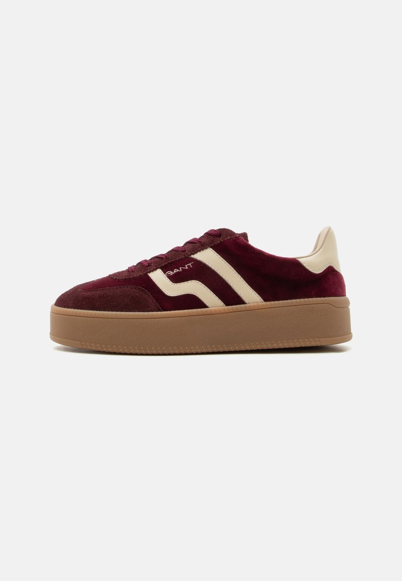 Baskets en daim bordeaux avec des bandes latérales beiges, semelle épaisse en caoutchouc marron, languette beige au talon et lacets bordeaux, vue latérale.