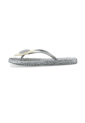 Sandalia plana tipo flip-flop trenzada plateada con tiras brillantes y una flor decorativa de color crema sobre un fondo blanco.