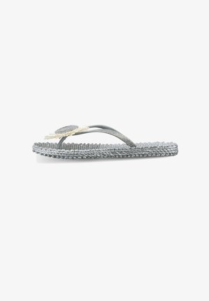 Sandalia plana tipo flip-flop trenzada plateada con tiras brillantes y una flor decorativa de color crema sobre un fondo blanco.