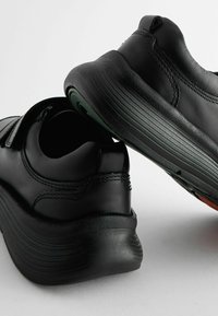 Chaussures en cuir noir avec un design arrondi, des semelles texturées et des accents de couleur contrastante à l'intérieur. Équipées de sangles à crochet et boucle.