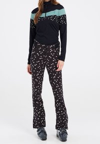 Zwarte skibroek met een wit bloemenpatroon, gecombineerd met een zwarte top met mintgroene horizontale strepen, in een aansluitend ontwerp en met een hoge halslijn.