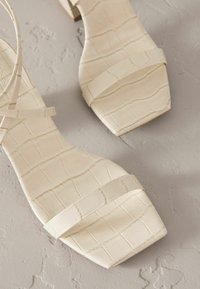 Helle beige, krokodilgeprägte Sandalen mit quadratischer Zehenpartie, ausgestattet mit zwei dünnen Riemen über dem Fuß und einem kleinen Blockabsatz.