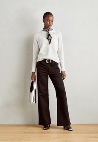 Gray knitted sweater with raglan sleeves, black wide-leg pants, a patterned scarf, shiny silver handbag, and pointed black shoes.