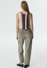Top a maniche corte lavorato a maglia multicolore con dettaglio di frange, abbinato a pantaloni beige con stampa leopardata. Scarpe nere flat completano l'outfit.