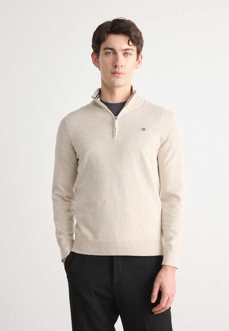 Suéter de forro polar beige con cuello simulado con cremallera, presenta mangas largas y puños acanalados. Logo sutil en el pecho.
