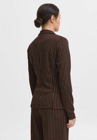 Blazer marrone a righe sottili realizzato in tessuto strutturato, con una vestibilità su misura e rever a scollo a V, visto da dietro.