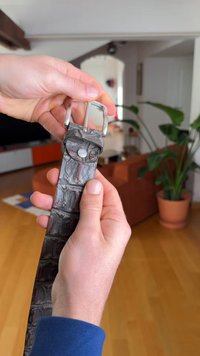 Ruskea krokotiilimallinen nahkavyö, jossa on hopeanvärinen metallisolki. Pintakuvio on yksityiskohtainen, kiiltäväpintainen ja hienostuneesti ommeltu.