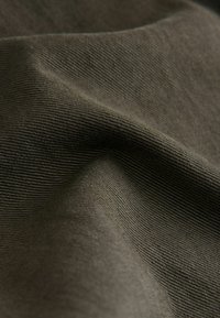 Texturiertes olivgrünes Gewebe mit feinen, parallelen Rippungen, das eine glatte Oberfläche und einen leichten Glanz aufweist.