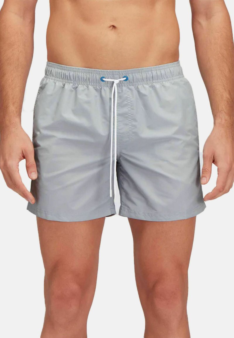 Pantaloni da bagno grigi con vita elastica e cordino, indossati da un uomo in piedi, che mostrano un look casual pronto per la spiaggia.