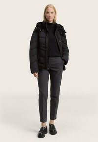 Zwarte pufferjack met een hoge kraag, ritssluiting en drukknoopjes. Donkere broeken en chunky zwarte loafers maken de outfit compleet.