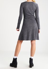 Szara sukienka z długim rękawem, wykonana z teksturowanej tkaniny, rozszerzająca się od talii. Noszona z czarnymi botkami za kostkę i białymi skarpetkami. Prosty, dopasowany krój.