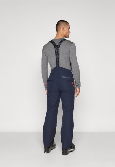 Marineblaue Skihose mit verstellbaren schwarzen Trägern, ausgestattet mit Reißverschlüssen und roten Akzenten, gefertigt aus einem strapazierfähigen und wetterfesten Material.