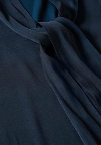 Tissu soyeux bleu foncé drapé et torsadé pour révéler une texture lisse et des plis doux avec des reflets subtils de lumière.
