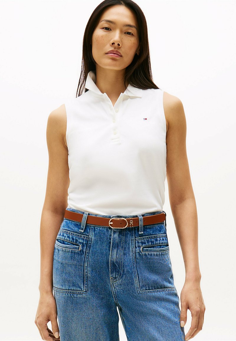 Witte mouwloze poloshirt met een kraag, gecombineerd met hoge blauwe denim jeans en een bruine riem met een zilveren gesp.