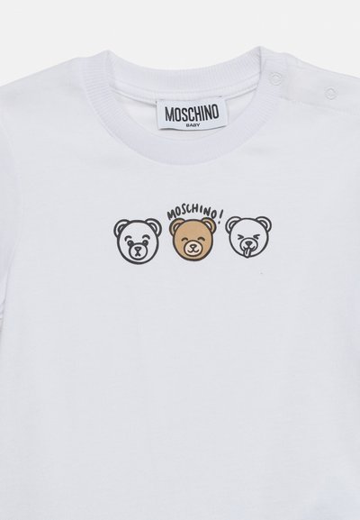 Λευκό παιδικό μπλουζάκι με τρία πρόσωπα αρκούδων σε σειρα, το μεσαίο καφέ με την επιγραφή «MOSCHINO!» από πάνω, και την ετικέτα της μάρκας στο γιακά.