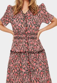 Šaty s květinovým potiskem, krátkými nabíranými rukávy, černým pozadím a červenými a růžovými vzory. Ozdobeny černým volánkovým pasem.