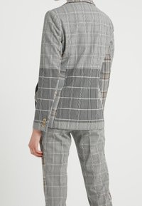 Blazer grigio a quadretti con pantaloni coordinati, caratterizzato da un motivo a quadri bicolore, design strutturato e bottoni dorati decorativi sulle maniche.