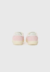 Baskets en suede rose avec une semelle en caoutchouc blanche, présentant une forme arrondie et une marque discrète au niveau du talon. Texture lisse, design minimal global.