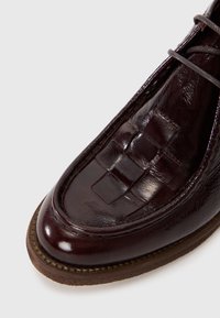 Brauner Lederschuh mit gewebter Textur im Obermaterial, runder Zehenpartie und einer kontrastierenden braunen Gummisohle. Schnürdesign.