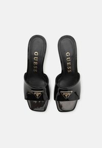 Black patent leather slide sandals with a wide strap, featuring a gold triangular logo accent and a smooth, high-gloss finish.