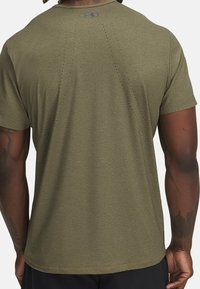 Maglietta sportiva a maniche corte in verde oliva, tessuto strutturato con occhielli traspiranti sulla schiena e dettaglio logo vicino allo scollo.