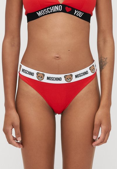 Sarkanas kokvilnas tanga apakšbikses ar baltu elastīgu jostu, uz kuras ir multfilmu lāča sejas un teksts "MOSCHINO". Gluda tekstūra un cieša piegriezums.