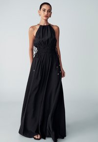 Black maxi dress made of lightweight fabric, featuring a halter neckline, cinched waist with drawstrings, and a flowing skirt.