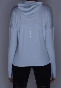 Felpa sportiva azzurra chiara con cappuccio, maniche lunghe e dettagli riflettenti sul retro. Texture liscia, design moderno e forma aderente.