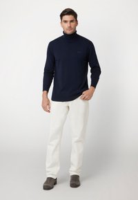 Maglione a collo alto navy realizzato in tessuto lavorato a maglia, con maniche lunghe e una vestibilità aderente, abbinato a pantaloni bianchi e stivali grigi.