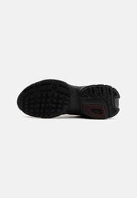 Sole of black athletic shoe with textured grip pattern and maroon accent on heel against plain white background.