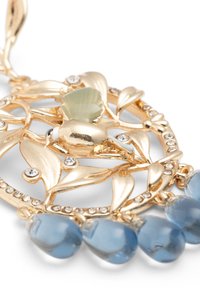 Gouden hanger met een bloemontwerp met bladeren, een lichtgroene schelpaccent en blauwe druppelstenen eronder. Rhinestone details zijn inbegrepen.