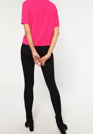 Leggings neri aderenti con una texture liscia, abbinati a una maglietta corta rosa brillante con dettaglio della zip sul retro.