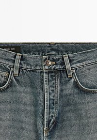 Denim jeans in medium blue with a classic five-pocket design. Features a button closure and sturdy stitching. Label reads “Massimo Dutti.”