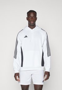 Weißer Kapuzenpullover mit schwarzen Seitenpanelen und drei schwarzen Streifen an den Ärmeln. Verfügt über eine Fronttasche und trägt das Adidas-Logo.