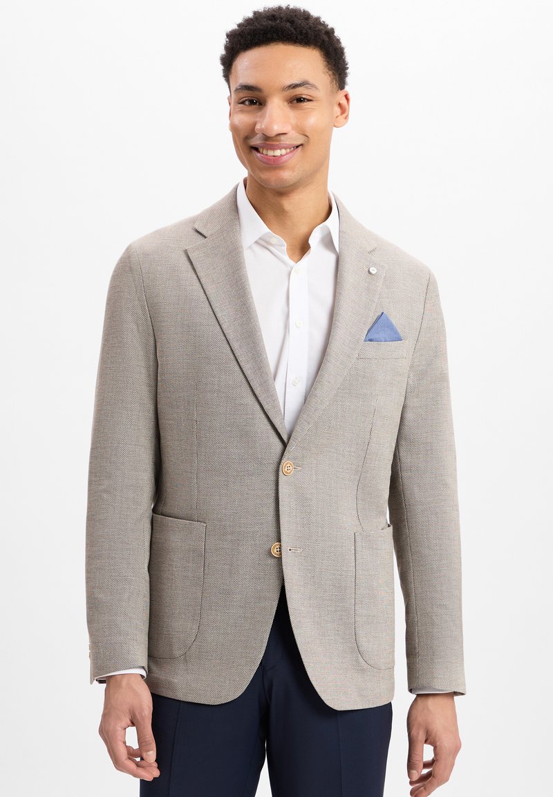 Beige textuur blazer met twee voorkleding zakken en houten knopen, gecombineerd met een wit shirt en een blauwe pochette.