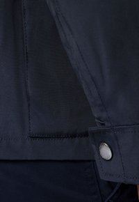 Granatowa kurtka z gładką fakturą, zapięciem na guziki i widocznym szwem na materiale o subtelnym splocie krzyżowym.