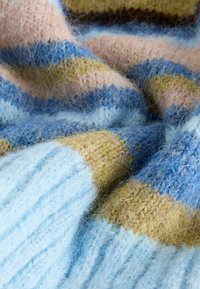 Pletená deka s pruhmi v pastelovo modrej, jemne ružovej, svetložltej a zemitom hnedej farbe. Textúrovaná priadza dodáva hĺbku a teplo.