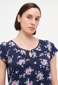 Top corto de manga corta en color navy con flores rosas y azules, escote con abertura y un pequeño logo. Tejido suave y corte relajado.