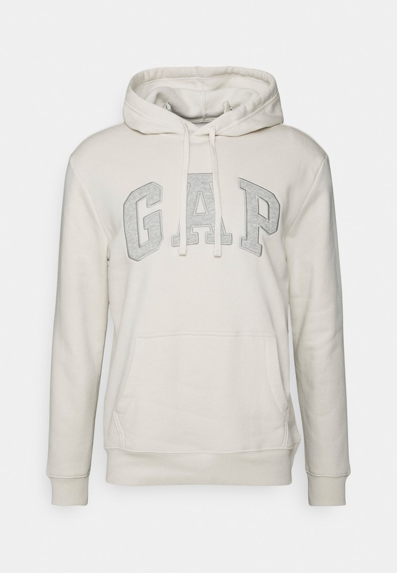 Sweat à capuche beige clair avec de grandes lettres grises "GAP" sur la poitrine, poche kangourou à l'avant et capuche avec cordon de serrage.