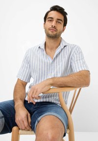 Camicia a maniche corte con righe verticali blu chiaro e bianche, dotata di button-up frontale, colletto rilassato e tessuto leggero.
