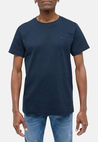 Námorně modré bavlněné tri�čko s krátkým rukávem a kulatým výstřihem, s jemným logem na hrudi a volným střihem. Nosí se s světle modrými džíny.