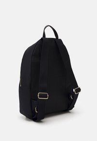 Czarny plecak z materiału o zaokrąglonym kształcie, z wyściółkowanymi paskami, uchwytem u góry, bocznym zamkiem błyskawicznym i akcentami w złotym kolorze.