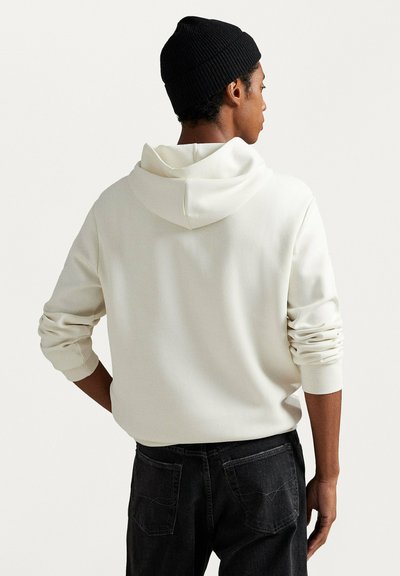 Felpa con cappuccio color crema con coulisse e tasca a marsupio. Polsini e orlo con texture, abbinati a jeans scuri. Design semplice e casual.