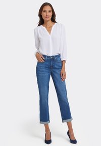 Vit långärmad blus med V-ringning, tillsammans med ljusblå denimjeans uppvikta vid muddarna, och mörkblå högklackade skor.