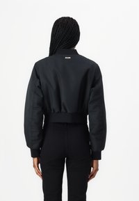 Afgekorte zwarte bomberjack met hoge kraag, geribbelde manchetten en logo-detail op de rug. Vlekkeloze stof met een minimalistisch ontwerp.