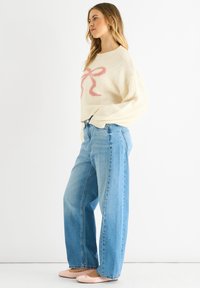 Cream sweater with pink bow design, loose fit, ribbed neckline. Light blue wide-leg jeans, smooth texture, paired with pink ballet flats.