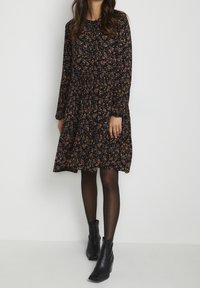 Robe noire à fleurs avec manches longues et taille froncée, portée avec des bottines. Présente un petit motif floral multicolore.