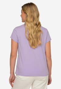 T-shirt lilas à manches courtes en tissu doux avec une coupe décontractée, présentant un col rond et un ourlet droit, associé à un pantalon clair.