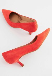 Červené semišové lodičky na vysokém podpatku s špičatou špičkou, nízkým podpatkem a hladkým vnitřním podšitím, které se vyznačují elegantním designem a minimem akcentů.